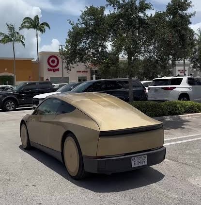 Beige futuristic two-door car parked in a shopping plaza lot near a Target store.