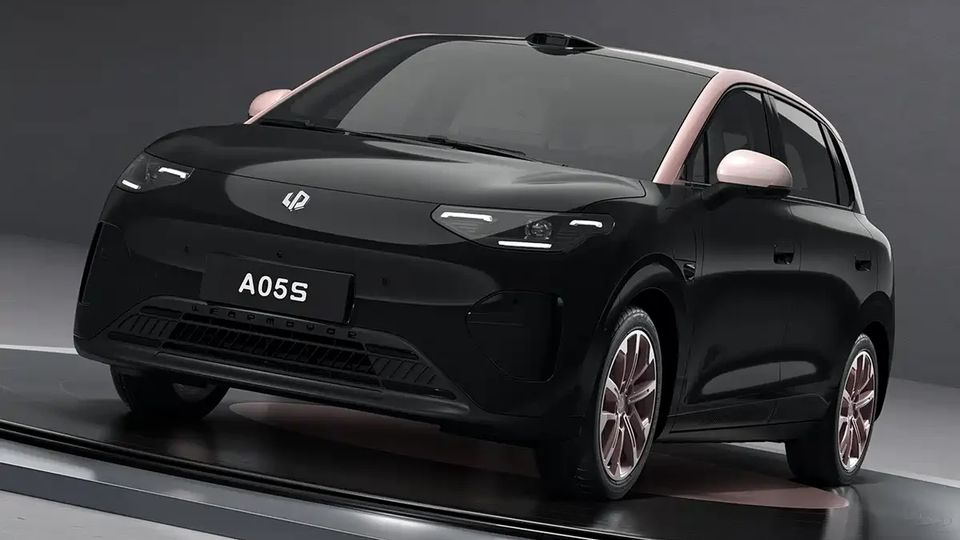 Angled view of a black compact hatchback with pink roof pillars, showing front grille and headlights, license plate reads A05S, on a showroom stand.