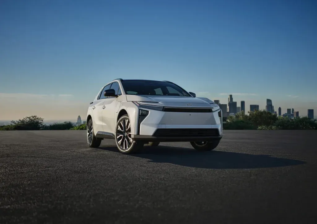 White modern SUV parked on a wide asphalt lot with a city skyline in the background.